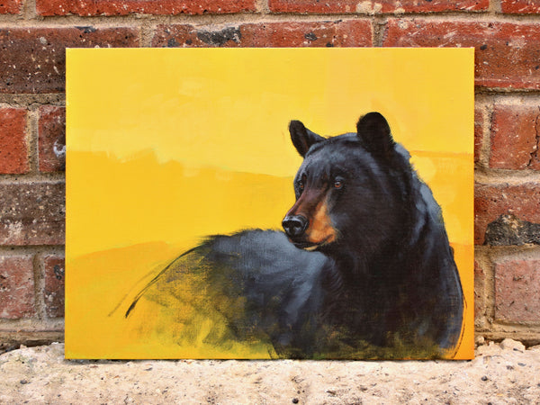 Black Bear painting with yellow background propped against a brick wall